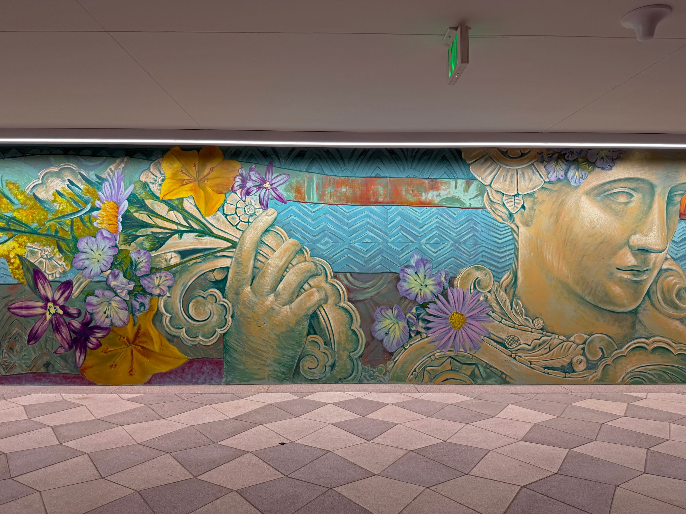 Section of the "Flourishing Structures" mural at Bloom on Third showing a classical sculpted face beside a hand holding purple and orange flowers