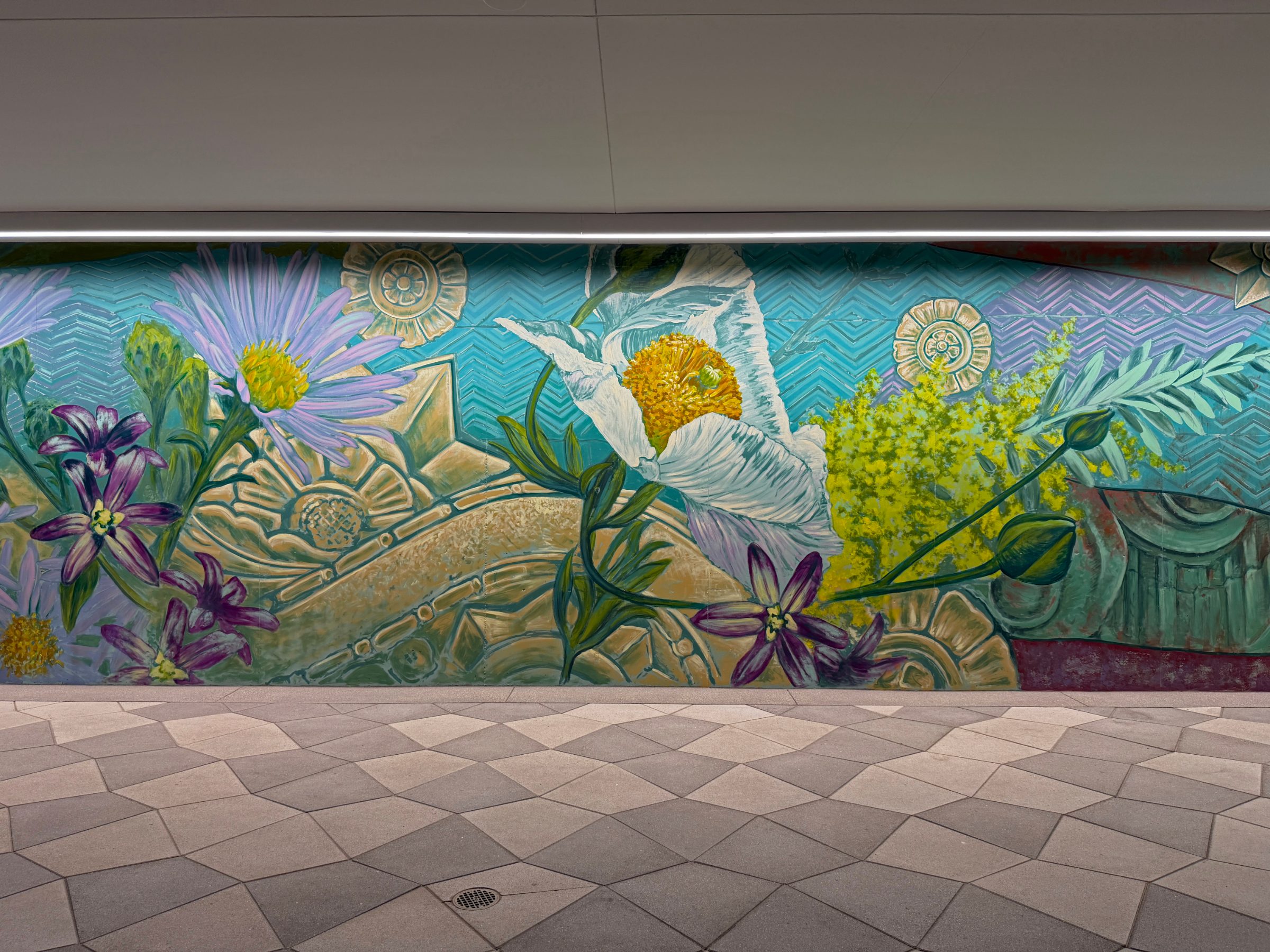 Section of the "Flourishing Structures" mural at Bloom on Third with purple asters, a white lily and yellow mimosa over teal scrollwork