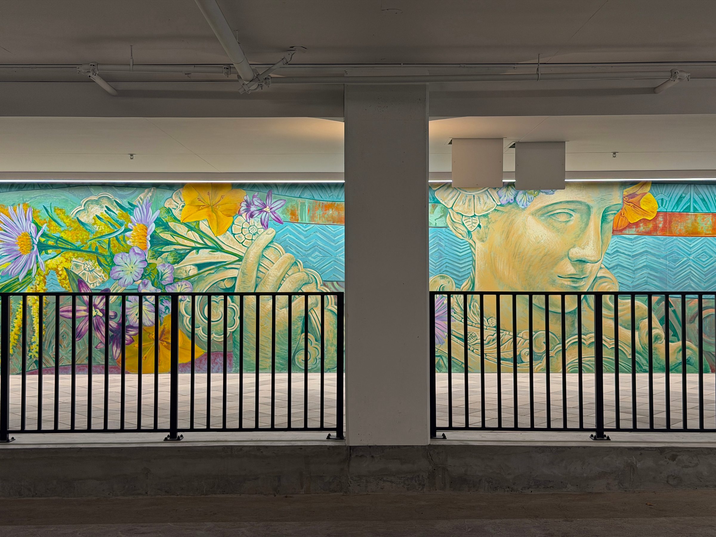 "Flourishing Structures" mural at Bloom on Third seen from the parking level behind a black railing and concrete column